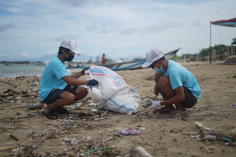 Two volunteers picking up garbage from a beach and placing it into a bag. 