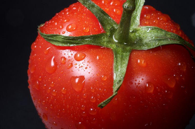 A close up view of a big, red tomato with drops of water on it.