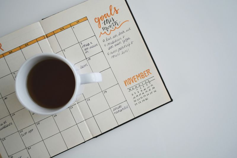 A diary with goal settings is lying on the table, and a cup of coffee is placed on the diary.