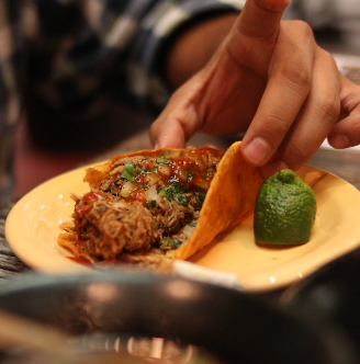A man picking up a birria taco from a plate. 