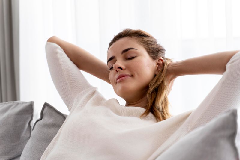 A women relaxed sitting on a sofa, with her hands behind her head.