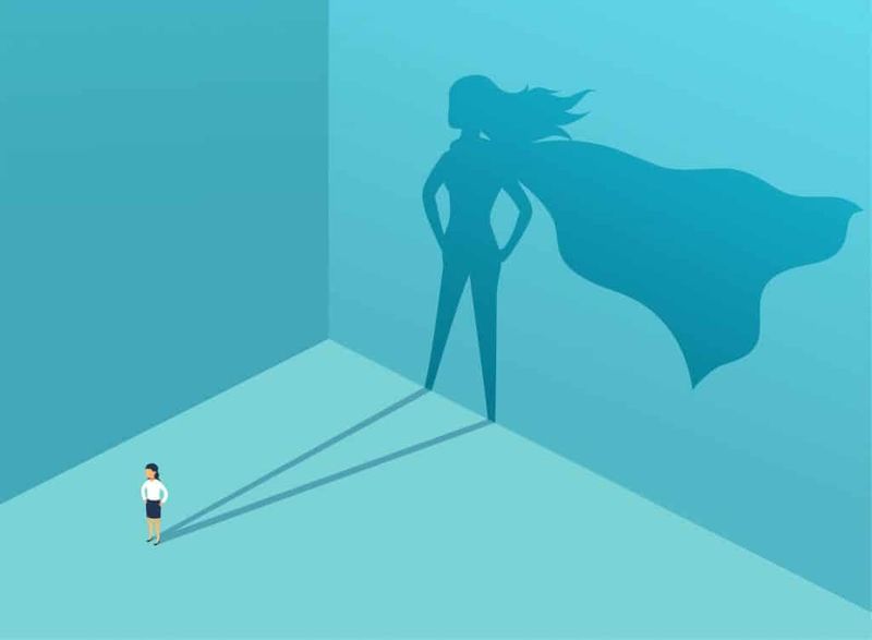 Woman casting a shadow behind her. Her shadow has a superhero cape.