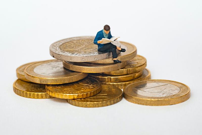 Little man reading while sitting on a stack of large gold coins 