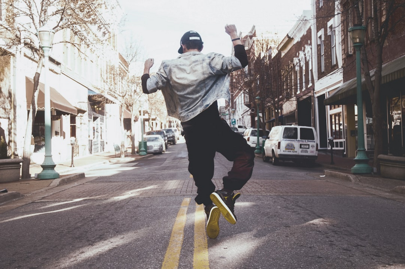 A young person on the street jumping in the air with their hands up in celebration.