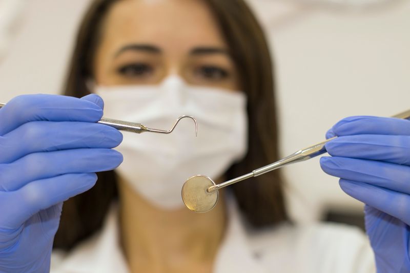 Image of a woman wearing a mask and holding dental tools.