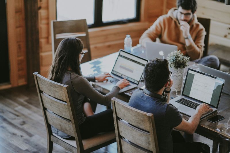 A shared workspace with three colleagues at the table, each working on their own laptops.