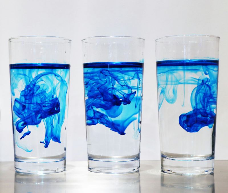 Three glasses of water with blue food dye mixing into the water.