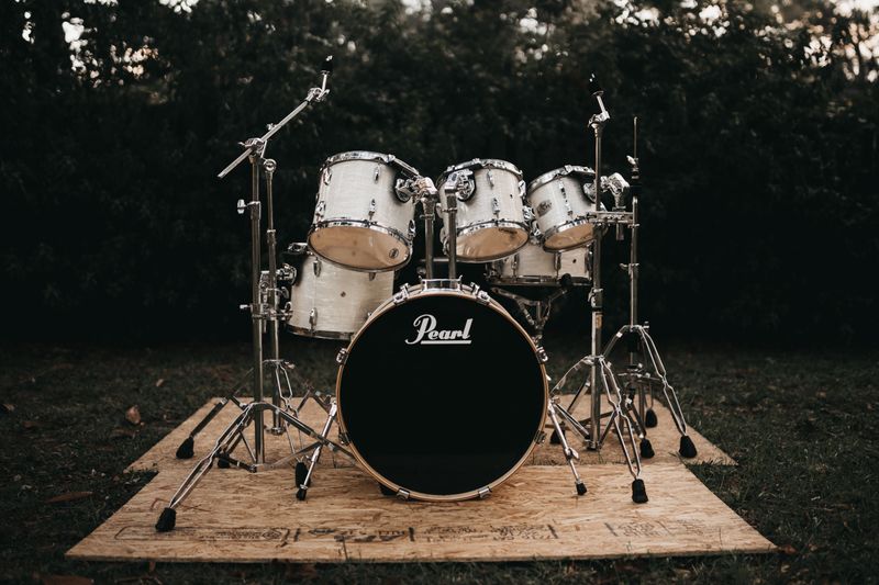 A Pearl 5 piece drum kit on a wooden base set up in a yard.