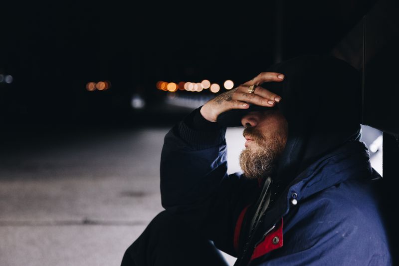 Man sitting alone on sidewalk cradling his forehead in his hand.