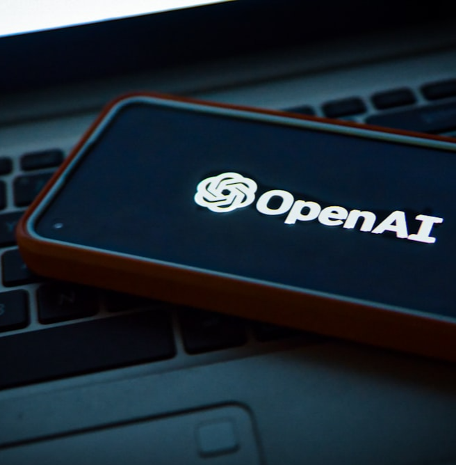 A cellphone on a laptop keyboard with OpenAI's app being loaded on the screen.