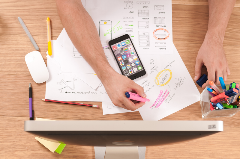 Papers, a phone, markers, pen, computer screen out on a desk with person highlighting.