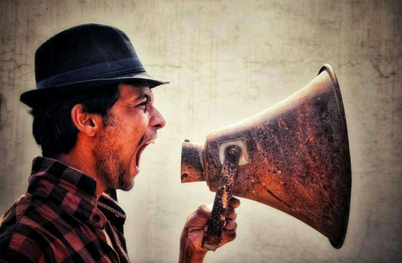 A person with a hat yelling into a loudspeaker.