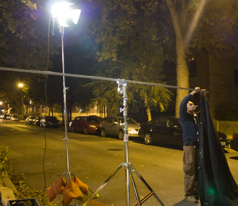 Grip setting up equipment at night in the street.