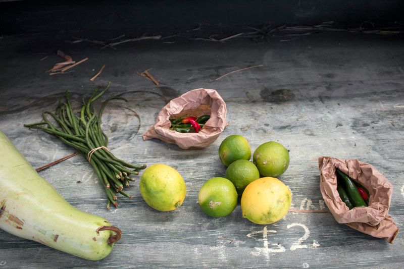 A rustic table with produce on it: squash, chives, limes, lemons, and brown paper bags filled with peppers.