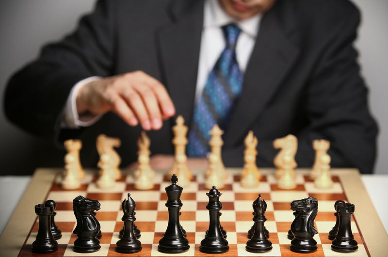 A chess board showing all of the different pieces on the board. A player in a suit makes the first move.