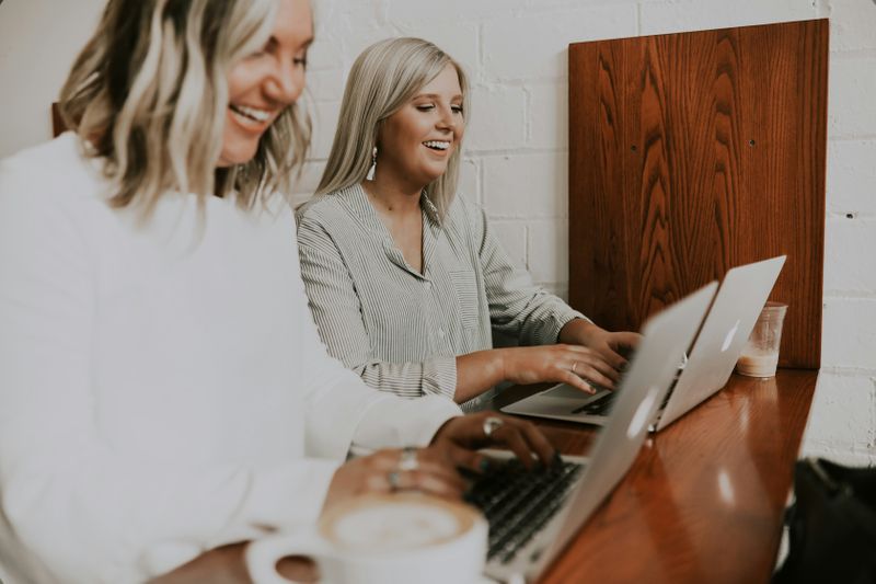 Two women typing on their Macbooks at work, looking confident and calm. 