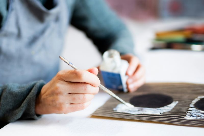 A person painting white paint on a striped black and beige pattern, next to black painted circles.