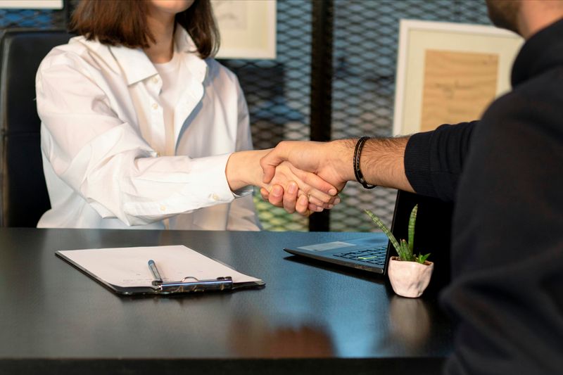 A woman and a man shaking hands at a job interview.