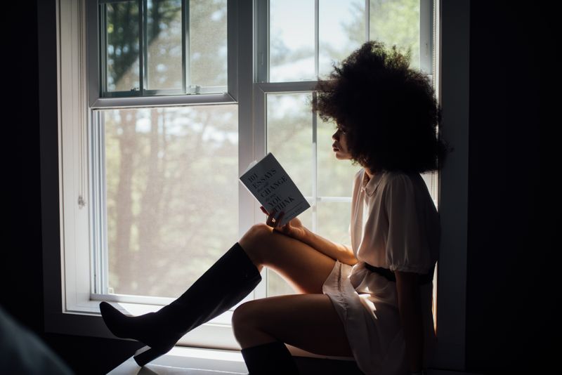 A woman seated by a window, reading a book.