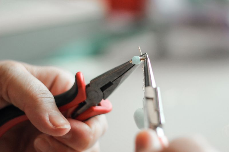 A person making handmade jewelry with a set of pliers.