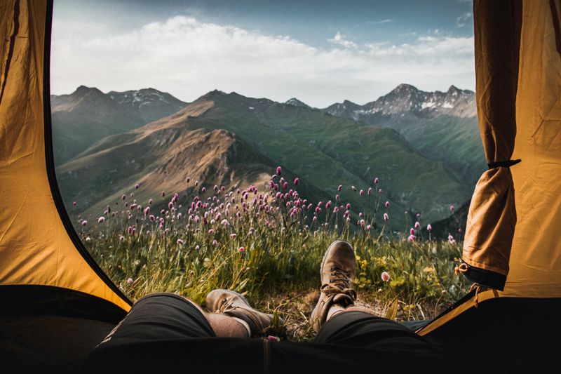 A person hangs their feet out of a tent facing a mountain view