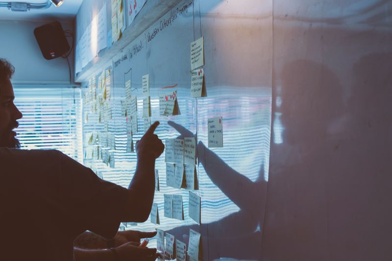 Photo of a man pointing at one post-it in a collection of post-its that are up on a whiteboard, symbolizing planning