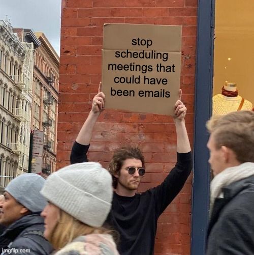 A man holding a cardboard sign in front of a crowd. It reads: stop scheduling meetings that could have been emails.