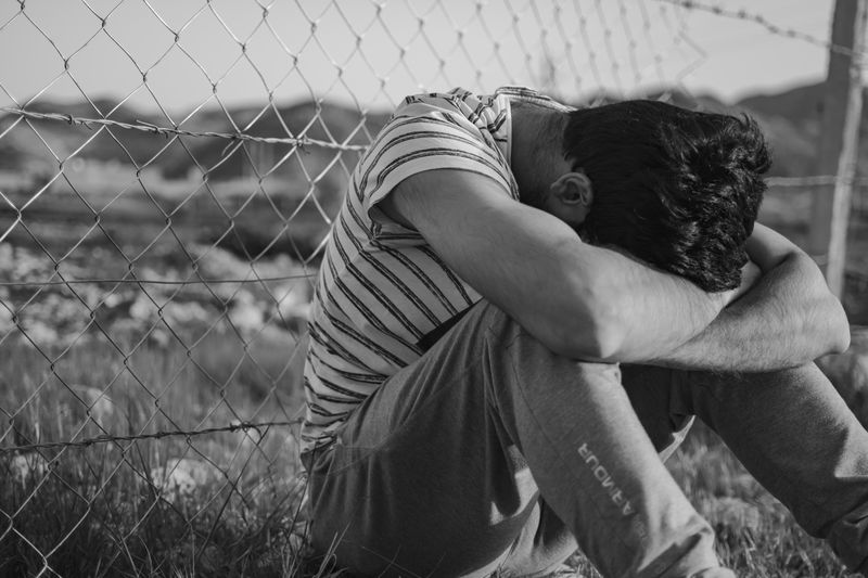 Man with head down sitting by a fence