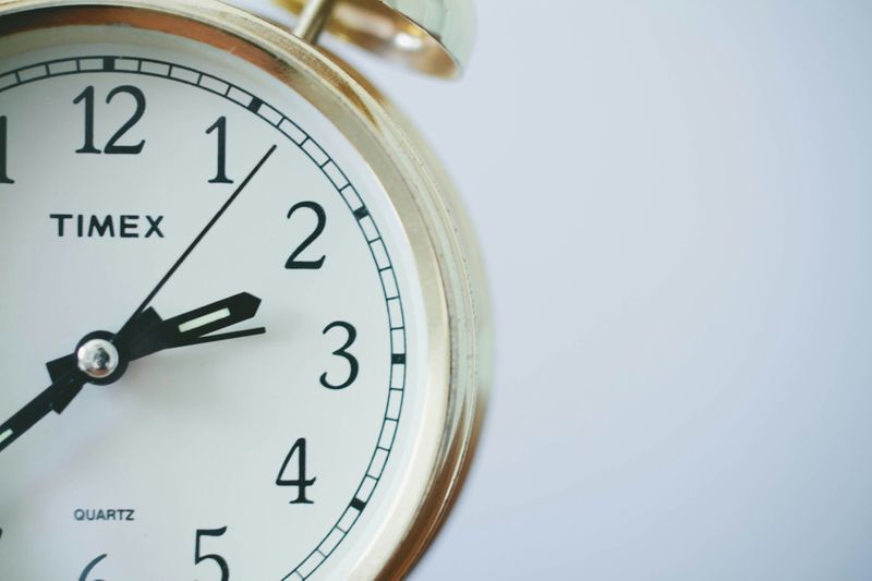 A close up of an alarm clock with the minute hand pointing at 3 o'clock.