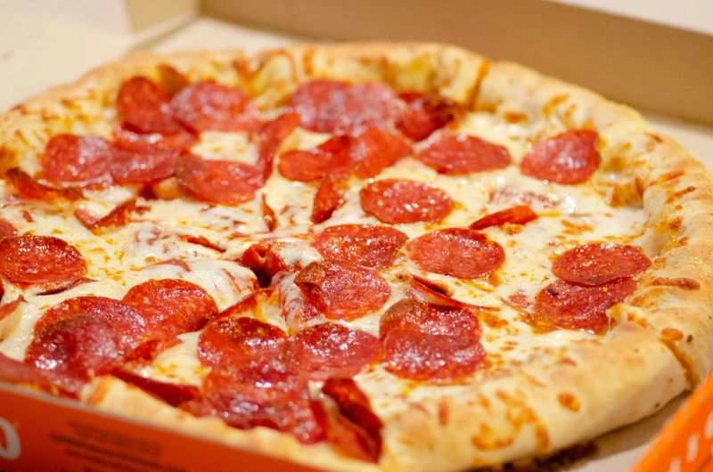 Pizza with cheese, pepperoni, and thick crust in an orange, cardboard delivery box.