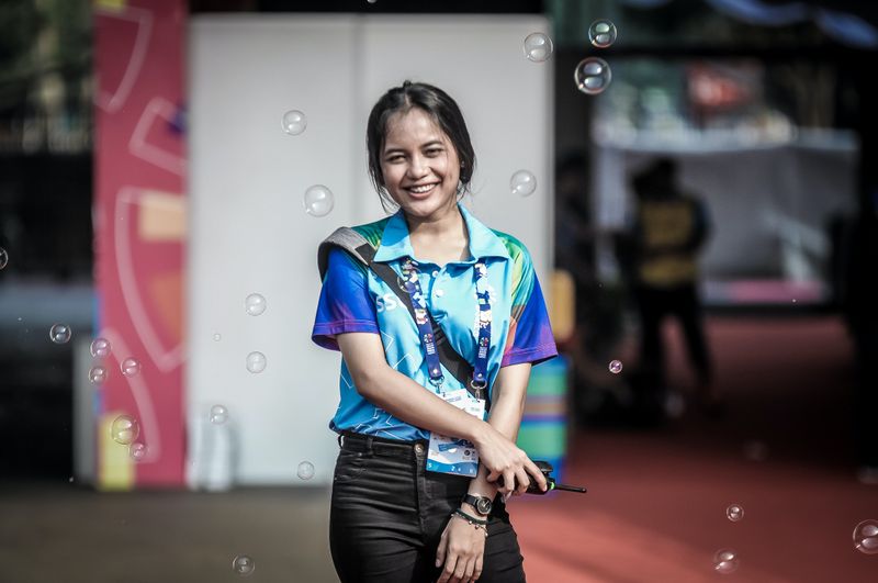 A volunteer wearing a lanyard and holding a walkie talkie. Soap bubbles float in the air around her.