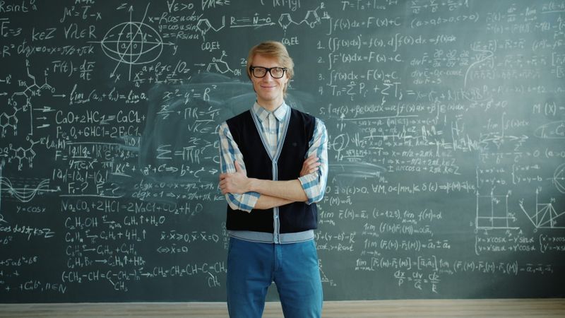 A confident looking teacher in front of a chalkboard.