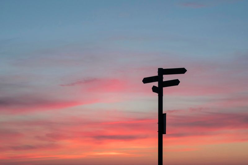 A single signpost with multiple signs pointing in various directions against a sky at sunset.