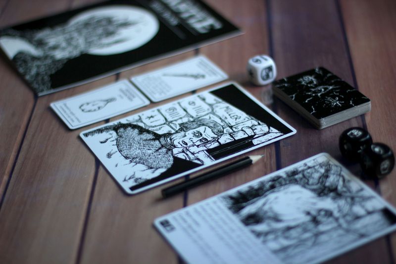 A gothic horror themed board game with all black and white cards, dice, and pieces