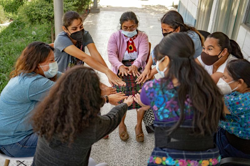 Eight women forming a circle with hands extended towards each other.