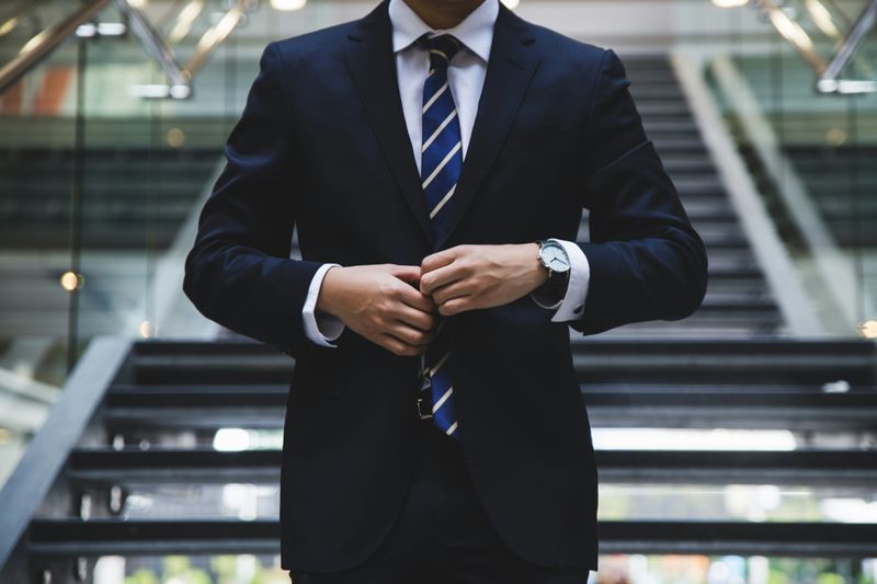 A person in professional clothing buttoning up blazer.