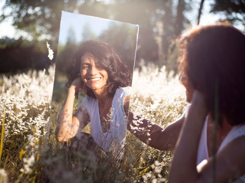 A person sitting in a group of flowers while smiling at herself in the mirror. 