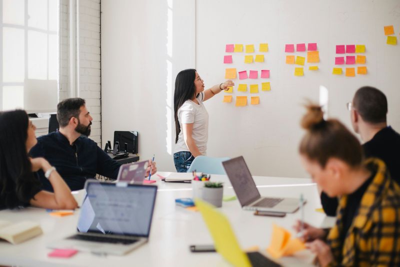 People having a meeting and looking at a whiteboard with sticky notes on it. 