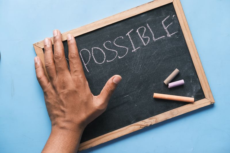 A chalk board with part of the word impossible covered by a hand.