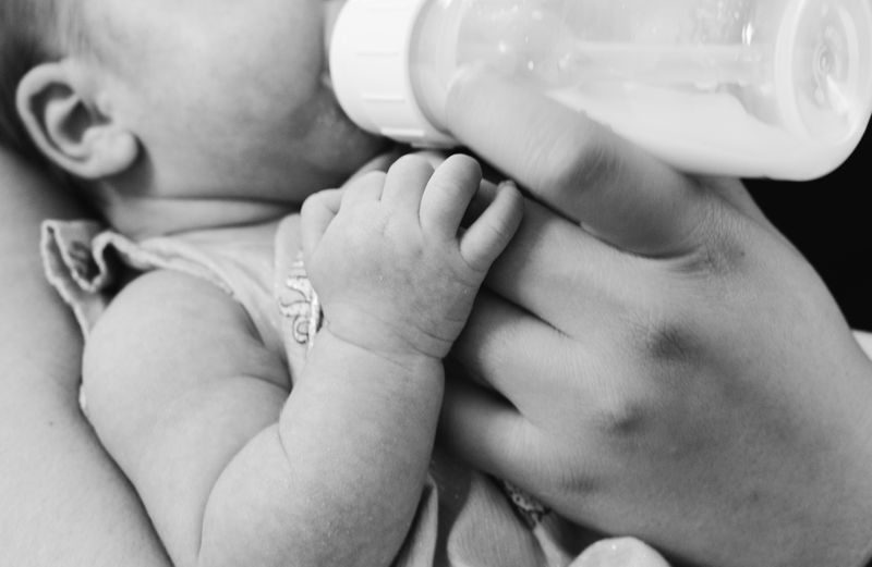 A black and white image zoomed in of a parent feeding their baby with a bottle. 