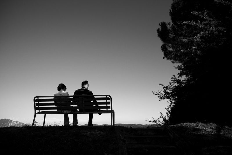 Two people in a situationship sitting side by side on a park bench.