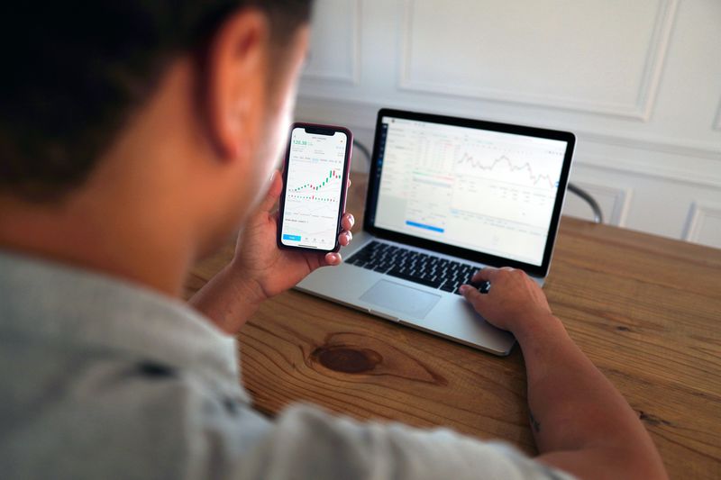 A guy looking at his laptop and phone, researching market data.