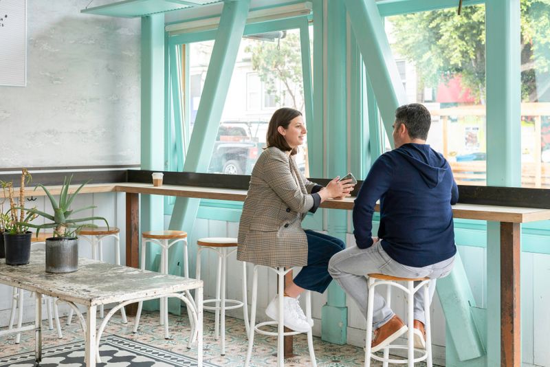 Two people are sitting at a café, smiling and talking.