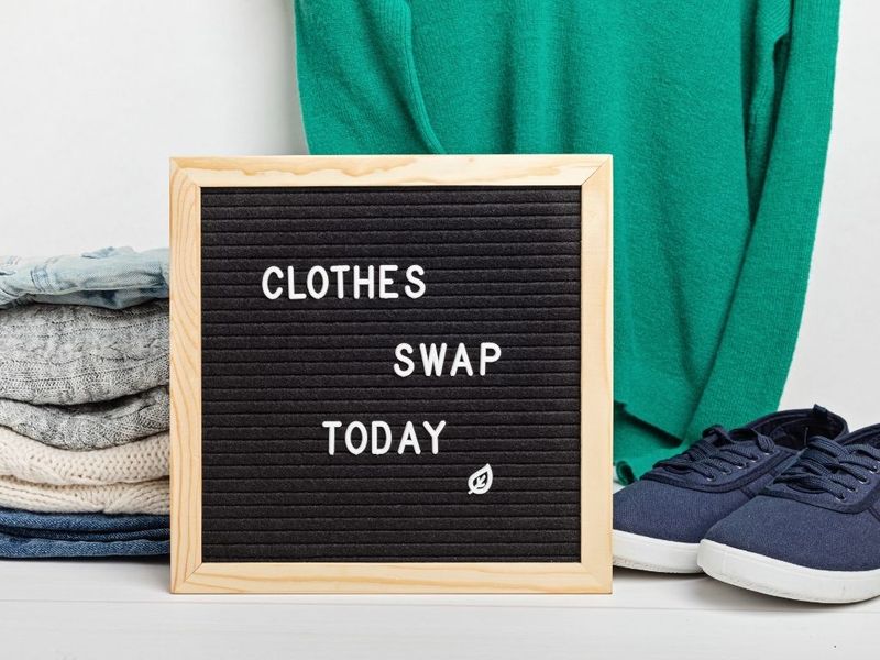 Clothes and shoes positioned around a letter board that reads 'clothes swap today.' (via: Canva)