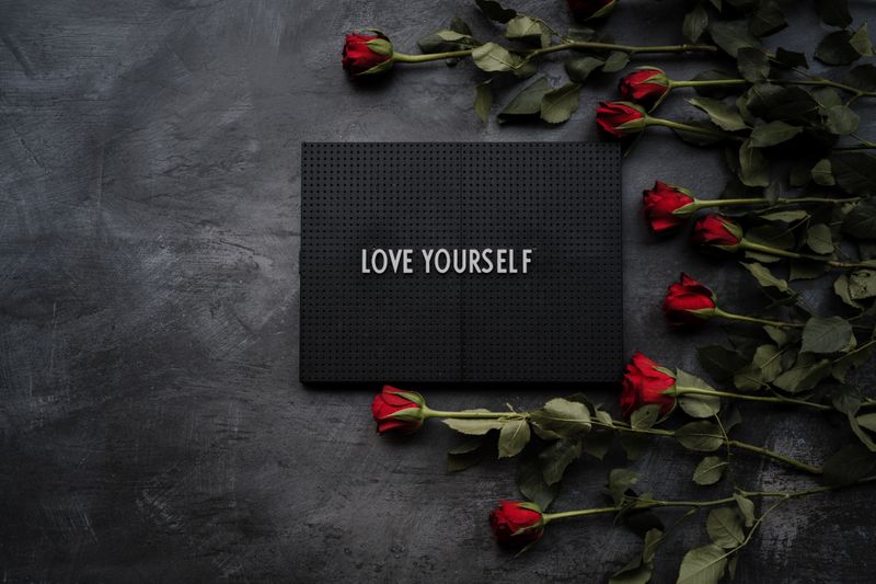 A black background with roses on the right side. In the middle there is sign with the words love yourself. 
