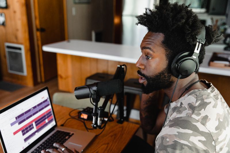 Image: Person talks into a recording mic while typing on the computer.