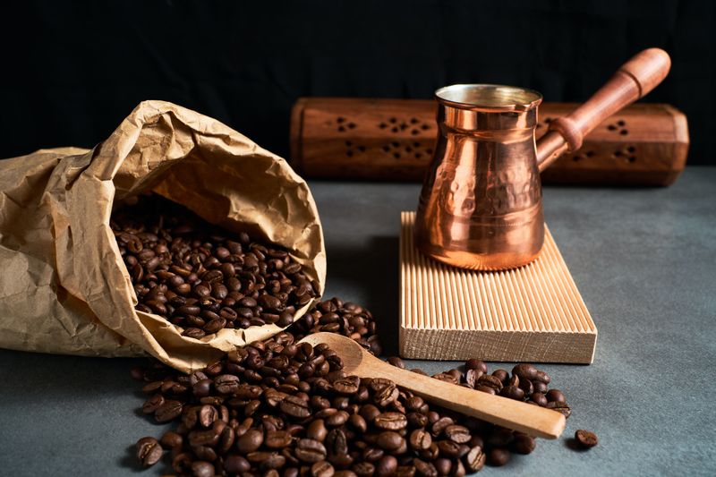 an image of coffee beans spilled from a bag next to a brass coffee pot