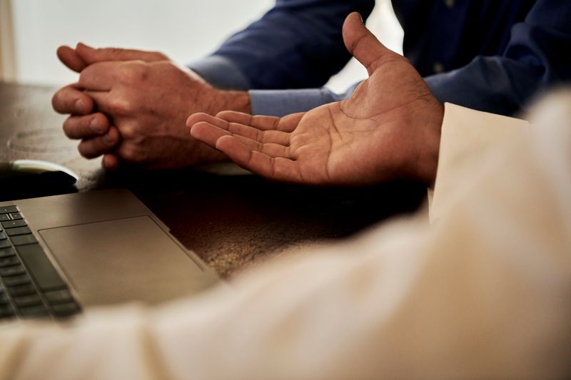 Two sets of hands. one reaching out in gesture, as other holds hands together