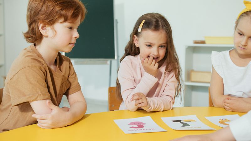 A group of young students engaging in a classroom activity with educational cards on a yellow table.