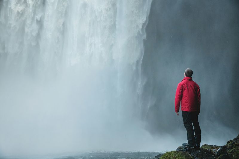 A person standing alone in front of a massive waterfall. 